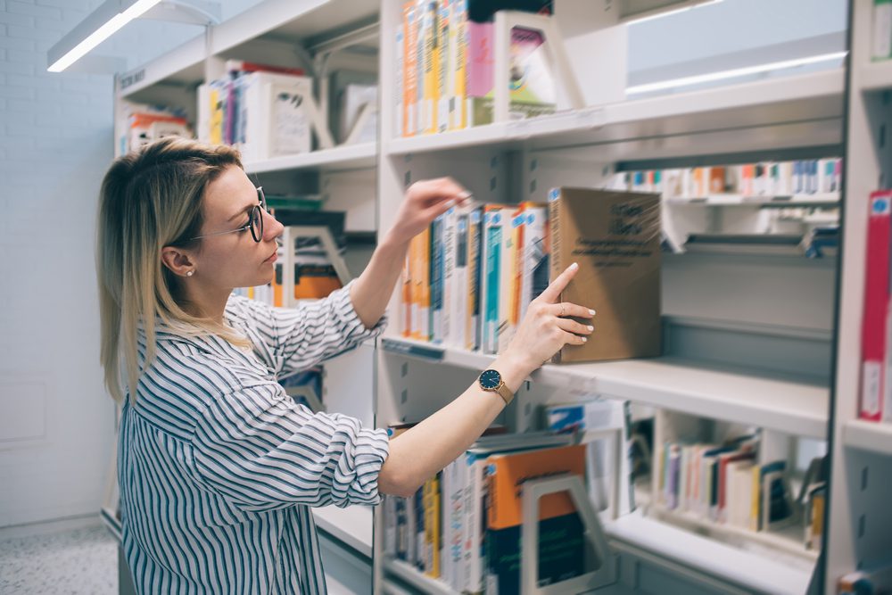 Young,Caucasian,Woman,Taking,Book,From,Shelf,In,Library,Searching Arbeitsunfall in Bibliothek Verletzenrente